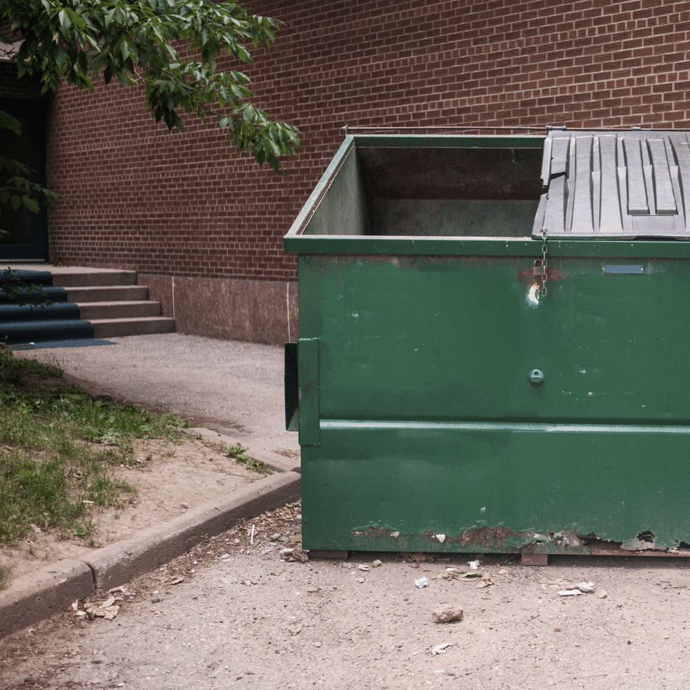 A green dumpster at the back of a brick building