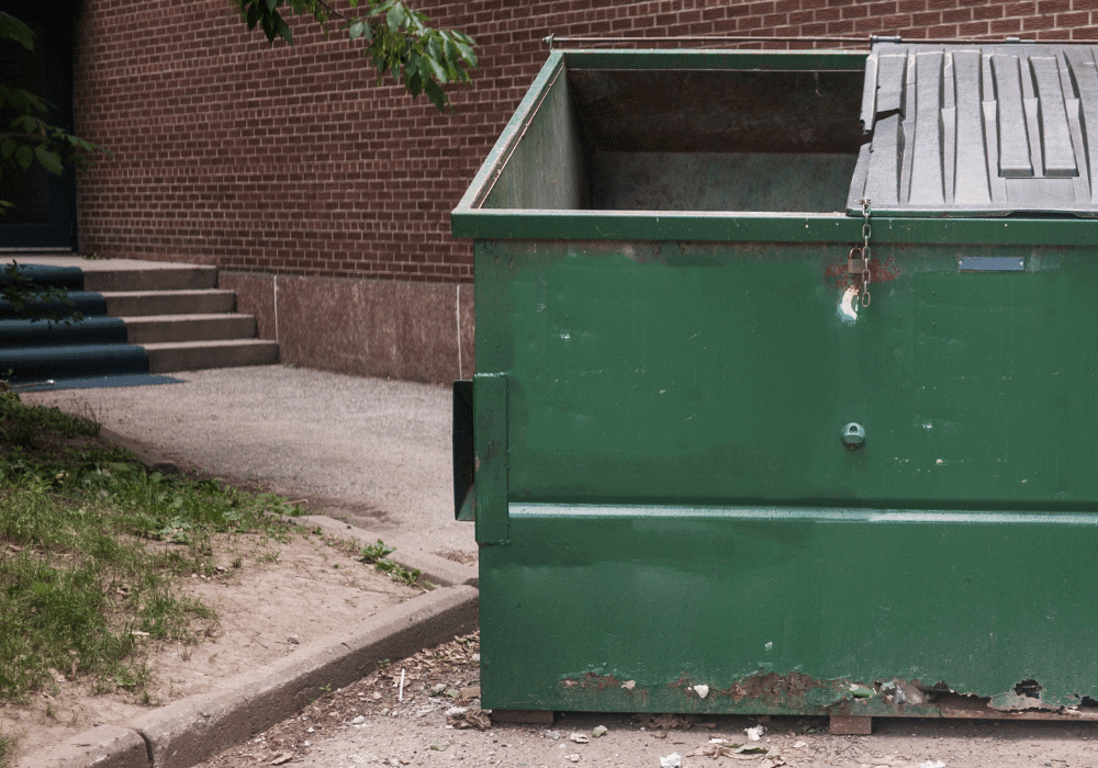 A green dumpster at the back of a brick building